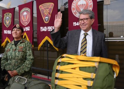 Ricardo Monreal saluda junto a una militar y equipo de paracaidismo durante una exhibición.