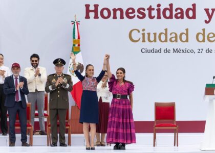 Claudia Sheinbaum y Clara Brugada levantan las manos unidas en el templete del Zócalo, acompañadas de autoridades.